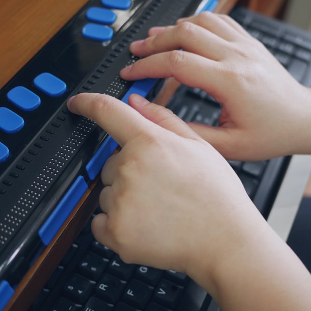 Close-up of hands using a braille display attached to a keyboard, demonstrating assistive technology for web accessibility.