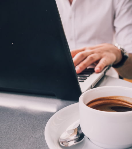 A person working on a laptop next to a cup of coffee