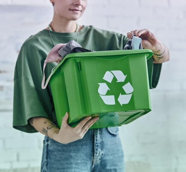 A person holding clothing items in a recycling bin