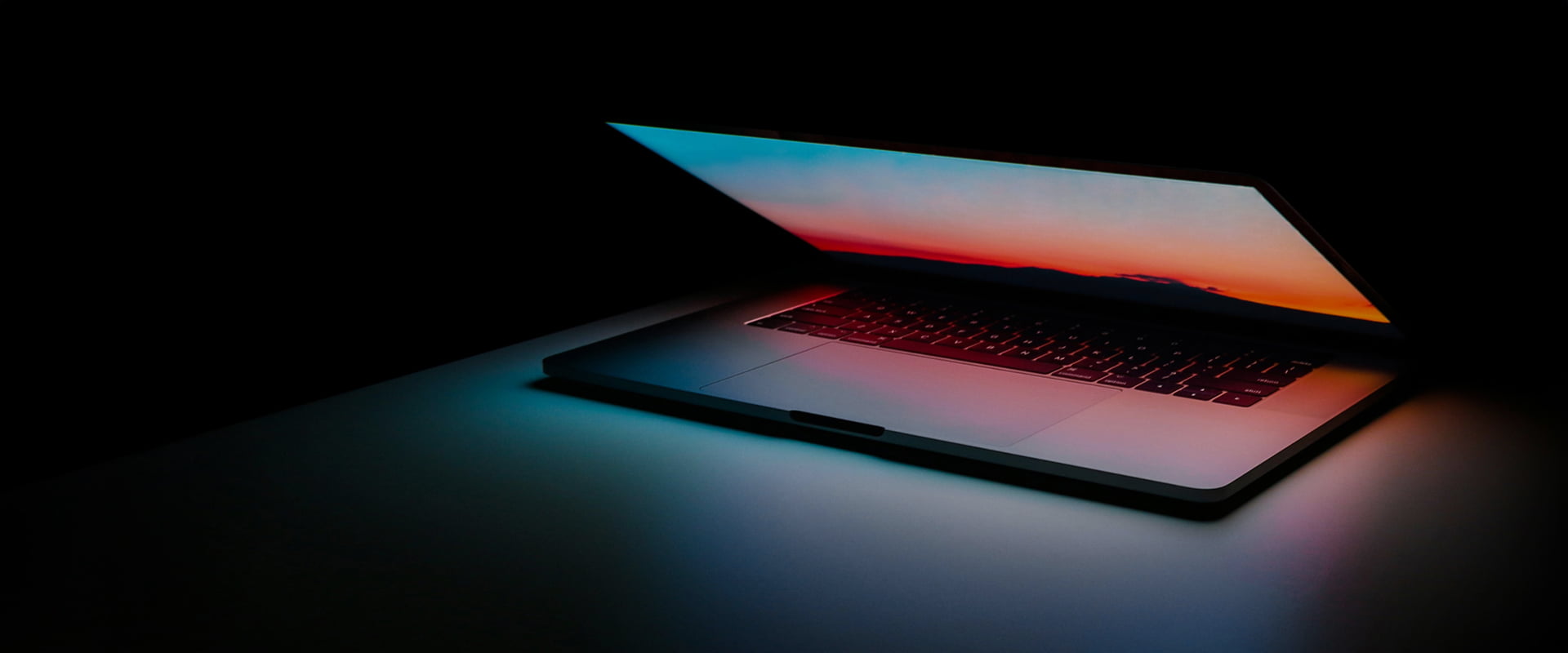 A half-opened MacBook in the dark on a white desk