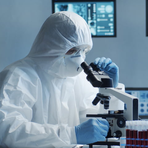 A scientist in a protective suit examining objects with a microscope