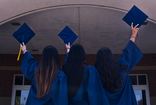 Three people wearing blue academic dresses rising hats