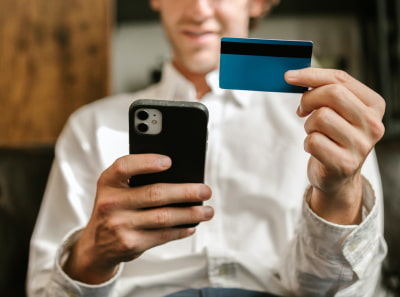 A person in a white shirt makes an online payment with a phone and a credit card