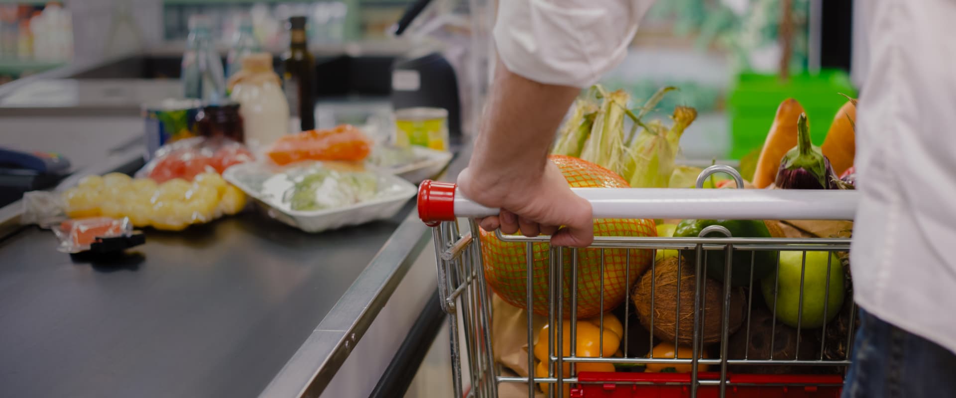 A person pushing a supermarket trolley loaded with fruits and vegetables