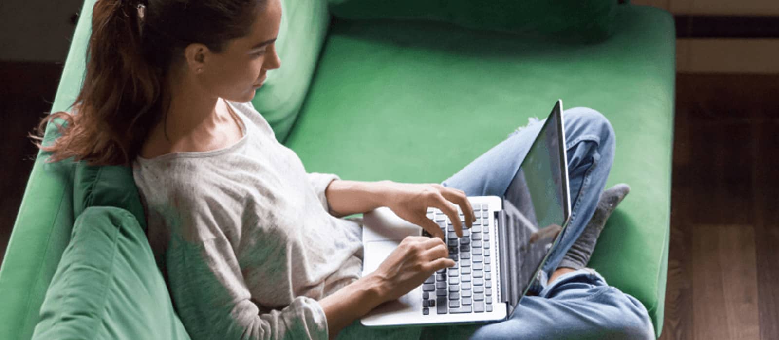 A woman on a green sofa working on a laptop